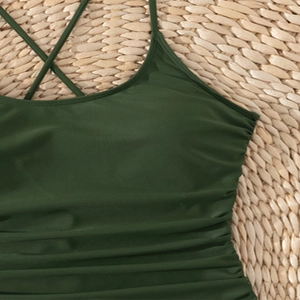Dark green one-piece swimsuit with cross back straps and pleated texture on straw mat