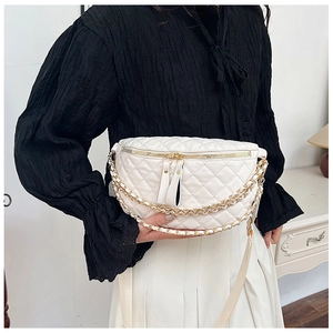Detail of white quilted crossbody bag featuring gold zippers and decorative metal chain