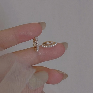 Elegant gold hoop earrings with small white pearls held for size demonstration