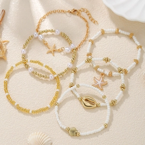 Close-up of Bohemian layered bracelets with gold starfish and shell charms and white beads