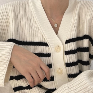 Detail of tulip shell pendant on striped knit cardigan showing the layered necklace style