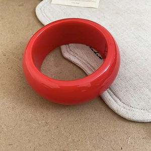 Detail view of a wide red resin bangle with a polished finish and thick circular design