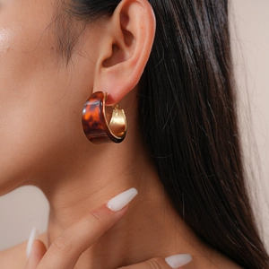 Close-up of tortoise shell resin C-shape hoop earrings with gold metal interior on model