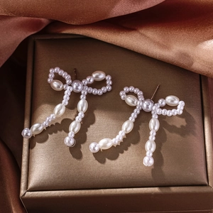 Elegant bow-shaped pearl tassel earrings with cascading white beads on golden tray