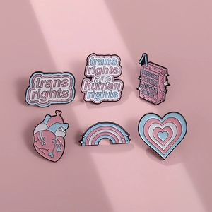 Transgender rights enamel pins set with heart and rainbow motifs on a soft pink background