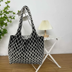 Detail of black and white wave pattern knit tote bag hanging on a white chair