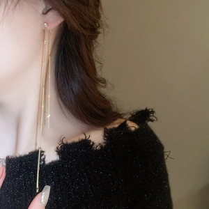 Close-up of golden long tassel chain earrings worn by a model with zircons