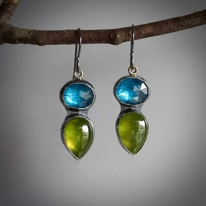 Pendientes vintage con gemas azules y verdes colgados de una rama de madera natural