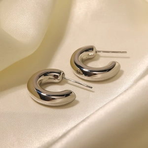 Polished silver C-shaped hoop earrings displayed on elegant beige silk fabric