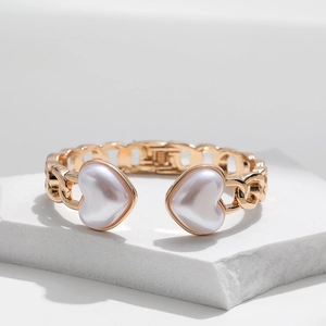 Golden chain link bracelet with heart-shaped pearls on a white stone pedestal