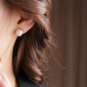 Close-up of elegant square pearl stud earrings with gold frame worn by a model