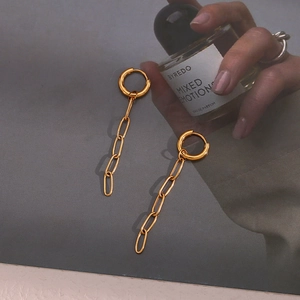 Detailed view of long gold chain link earrings paired with high-end perfume bottle
