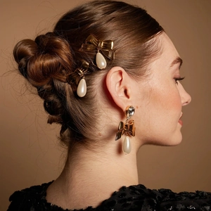 Detailed view of 18k gold butterfly hair clips and pearl drop earrings on a model