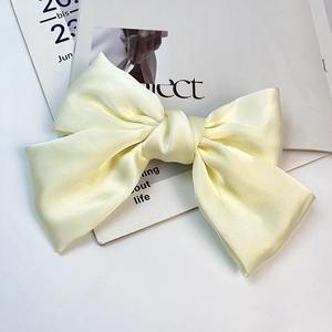 Close-up of a large pale yellow satin bow hair clip on a magazine backdrop