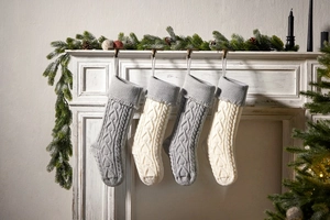 Knitted Christmas stockings with tassels hanging on a fireplace with pine cones