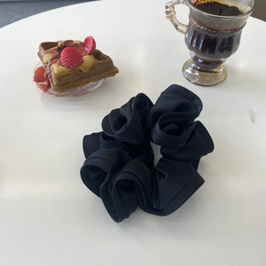 Detailed close-up of large black ruffled scrunchie with silk-like texture and soft pleats