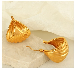 Detailed view of gold hoop earrings with shell ribbed texture on a soft beige background