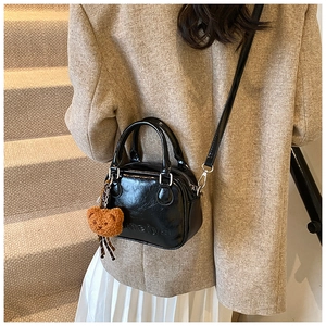 Detail of black mini crossbody bag with embossed lettering and a cute plush bear charm