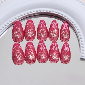 Sparkly pink almond press-on nails with decorative bows and glitter on a pearl tray
