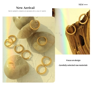 Detailed view of textured 18K gold plated hoop earrings on pebbles and wood base