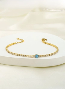 Close-up of gold titanium steel bracelet with a central blue gem and square zircon stones