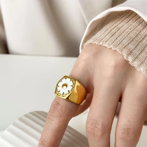 Close-up of a vintage gold daisy ring with white floral enamel on a model's hand