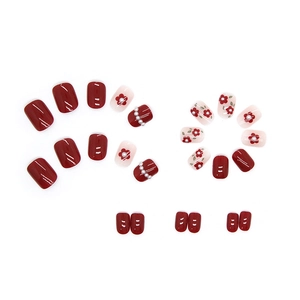 Red and white press-on nails set with pearl accents and floral designs on white background
