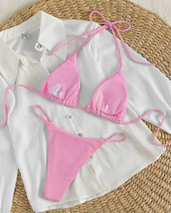 Detailed view of pink ribbed bikini set placed on white shirt with summer beach texture