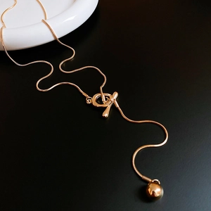Detail of gold snake chain necklace featuring a T-clasp and a polished ball pendant