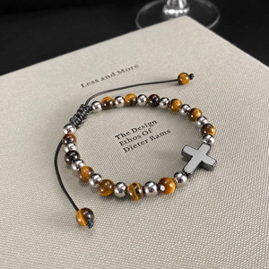 Dettaglio del bracciale con occhio di tigre e ciondolo a croce nera su un libro di design