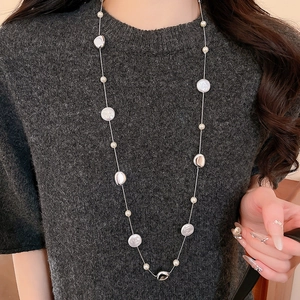 Detail of silver long sweater chain with baroque pearls on a gray knit sweater