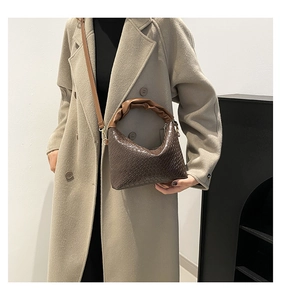 Detail of dark brown woven mini bag with ruched handle shown on a model's beige coat