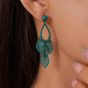 Close-up of matte dark green hollow leaf tassel earrings worn by a model