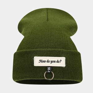 Détail du bonnet en maille vert foncé avec anneau métallique et écusson lettré