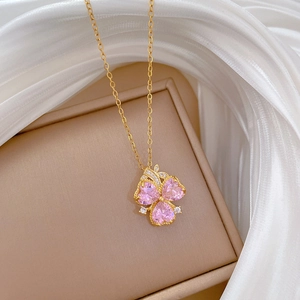 Close-up of golden clover necklace with pink heart-shaped stones on silk fabric