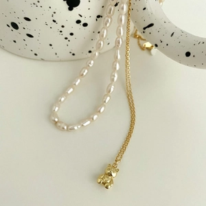Detail of layered gold bear pendant and baroque pearl necklace on a ceramic cup