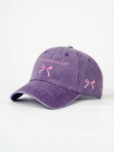 Detail of pink bow embroidery and 'I'm literally just a girl' text on a purple washed cap
