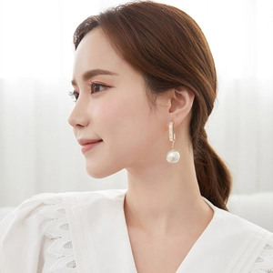 Detail of gold hoop earrings with white pearls and sparkling zircons worn by a model