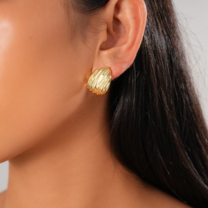 Boucles d'oreilles dorées texturées en forme de coquille portées par un mannequin