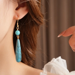 Dettaglio di orecchini boho con resina marmorizzata blu-verde e ganci in metallo dorato