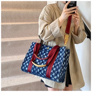 Side view of a large checkered denim tote bag with red handles shown in a lifestyle setting