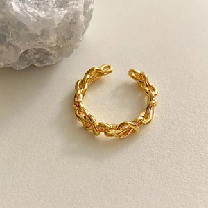 Detail of a vintage golden braided chain open ring on a beige textured surface