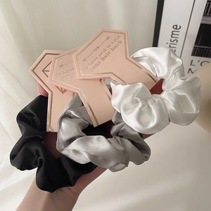 Three-piece set of satin scrunchies in black, silver and white on display cards