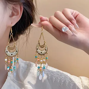 Dettaglio di orecchini boho con nappine, motivo floreale a mezzaluna e perline colorate