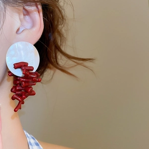 Close-up of circular shell earrings with red coral-like resin clusters on model