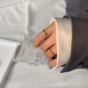 Detail of minimalist gold knot rings worn while holding a textured glass cup