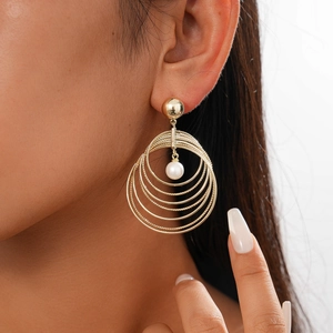 Close-up of golden multi-layer circular earrings with a centered faux pearl on a model