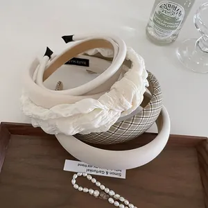 Detail of white pleated and plaid fabric headbands featuring a 'HAND MADE' inner label