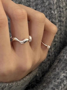 Macro detail of wave silver ring and pearl band set on grey knitted fabric background