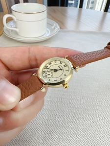 Close-up of gold watch with Roman numerals, beige dial and brown leather strap